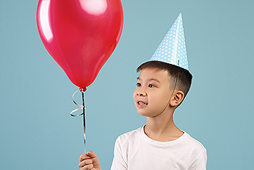 Child with red balloon and birthday party hat